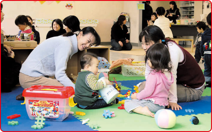 室内の遊び場で複数人の幼児と親が微笑みながら遊んでいる写真
